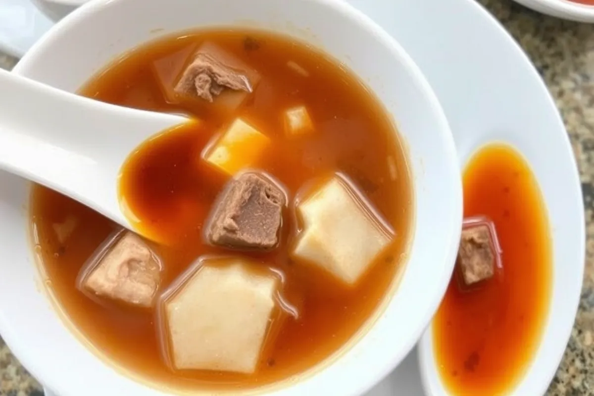 Image of pork-based Sinigang soup with visible layers of fat on the broth and a side of fish sauce, highlighting concerns over sodium and fat content.