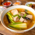 A steaming bowl of traditional Sinigang soup with vegetables and pork, highlighting its vibrant presentation and comforting appeal.