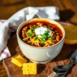 Bowl of deer chili topped with cheese, cilantro, and sour cream